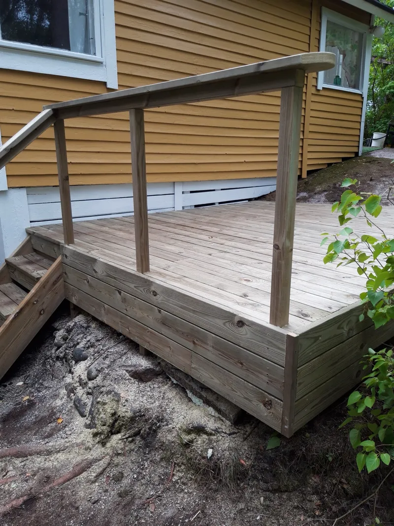 Uus terrass ja käsipuuga trepp kollase puitmaja küljes